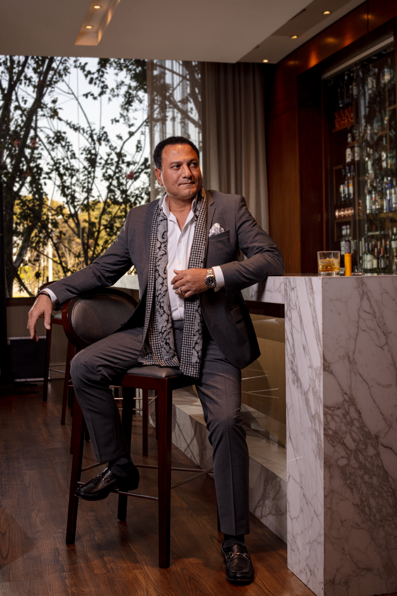 Mark Bastorous seated on a chair in a tailored grey suit within an elegant interior
