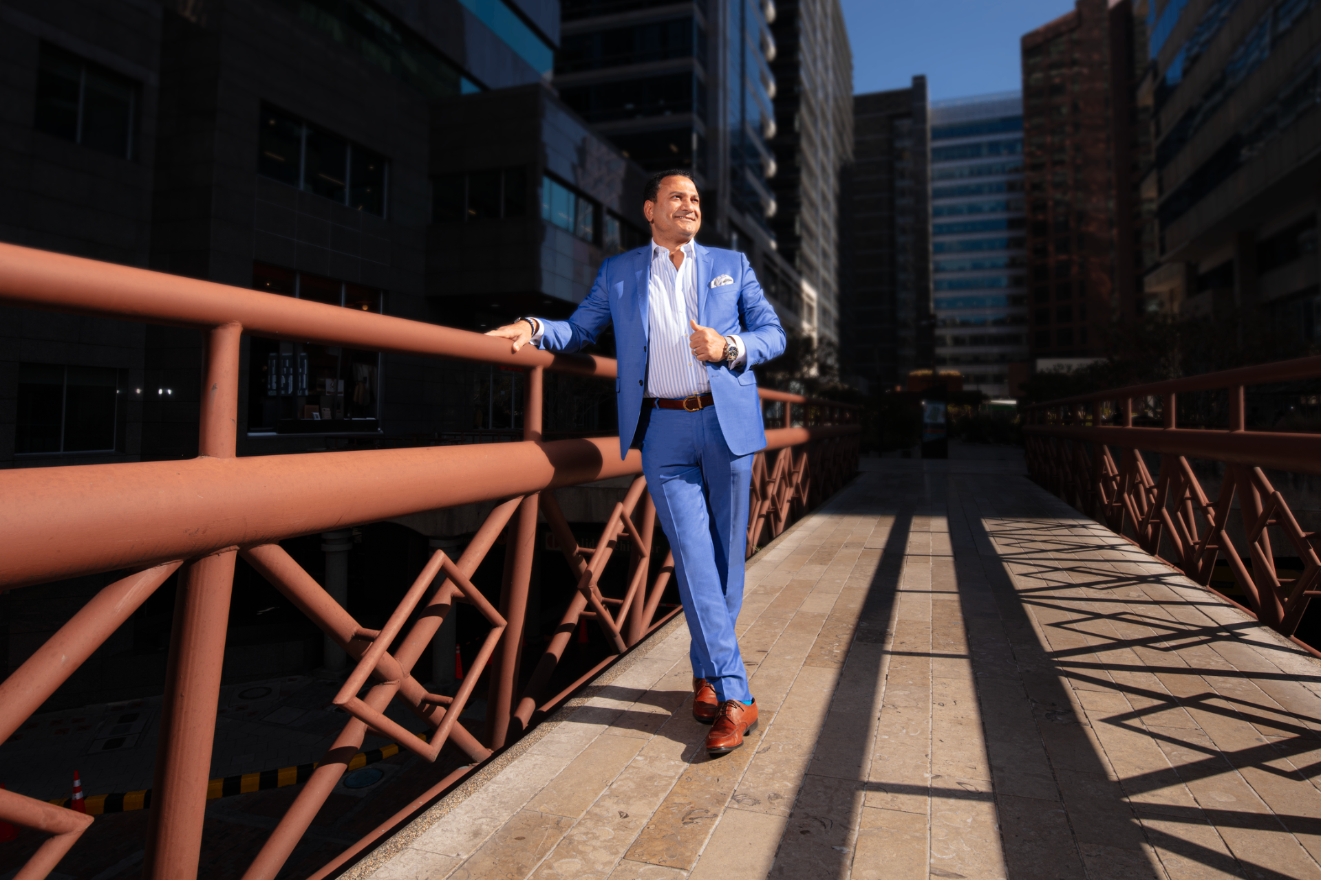 Mark Bastorous in a blue suit on a city bridge at golden hour, looking forward with quiet confidence
